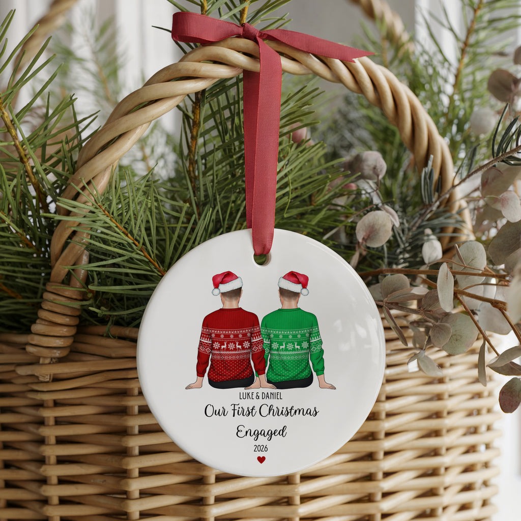 A round white ceramic Christmas ornament hanging from a red ribbon bow in a wicker basket, decorated with an illustration of two people in red and green sweaters and personalized text.